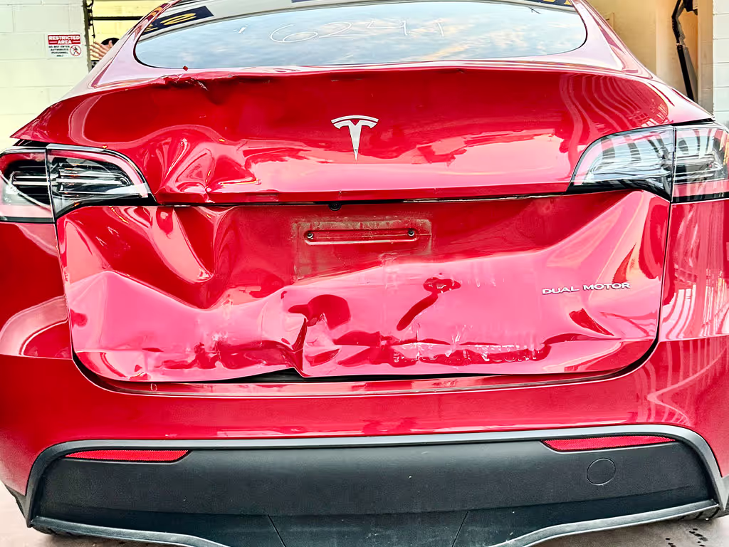 Rear view of a red Tesla Model Y with significant damage on the rear trunk and bumper.